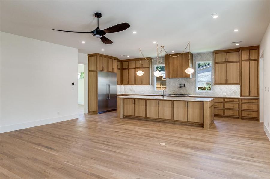 Kitchen featuring light wood-type flooring, a kitchen island with sink, built in fridge, tasteful backsplash, and a ceiling fan Kitchen featuring light wood-type flooring, a kitchen island with sink, built in fridge, tasteful backsplash, and a ceiling fan