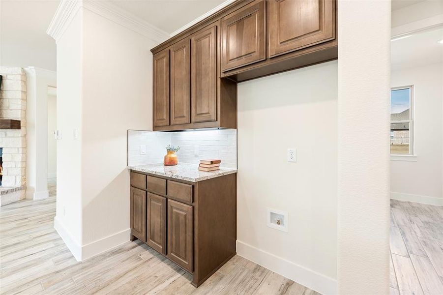 Kitchen with light stone countertops, crown molding, light wood-style flooring, backsplash, and a brick fireplace