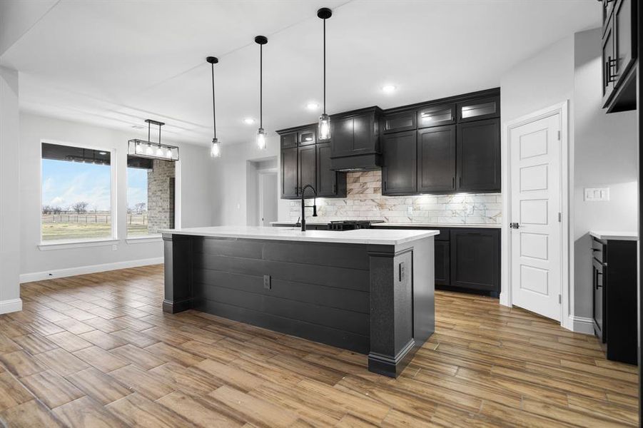 Kitchen featuring backsplash, a center island with sink, pendant lighting, and sink