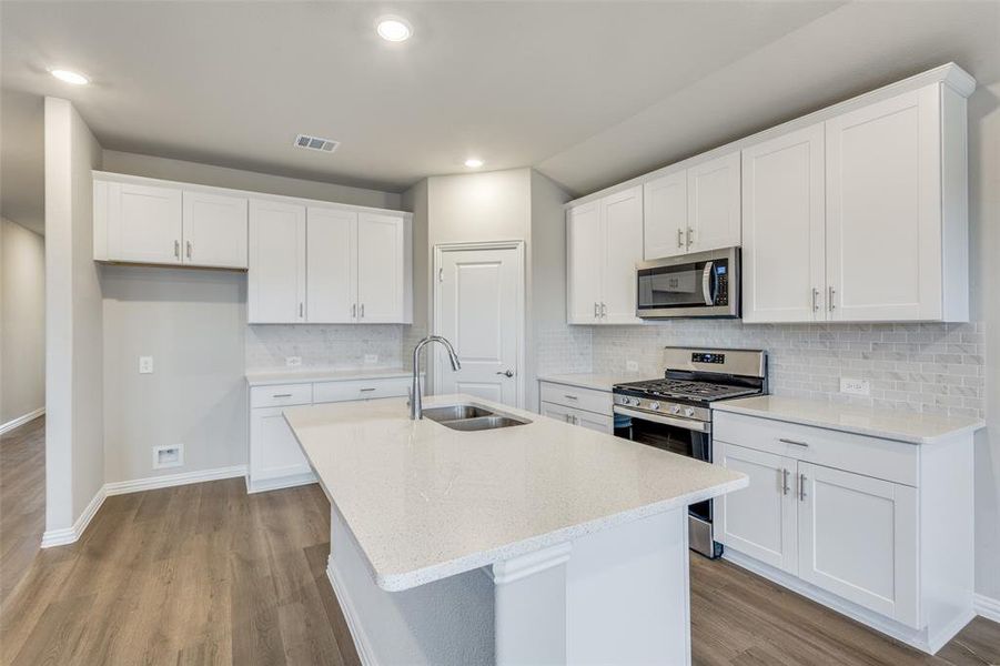 Kitchen featuring appliances with stainless steel finishes, white cabinetry, light stone counters, tasteful backsplash, and an island with sink