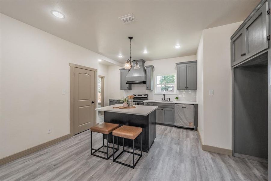Kitchen featuring a kitchen breakfast bar, backsplash, a center island, light wood-style floors, and light countertops