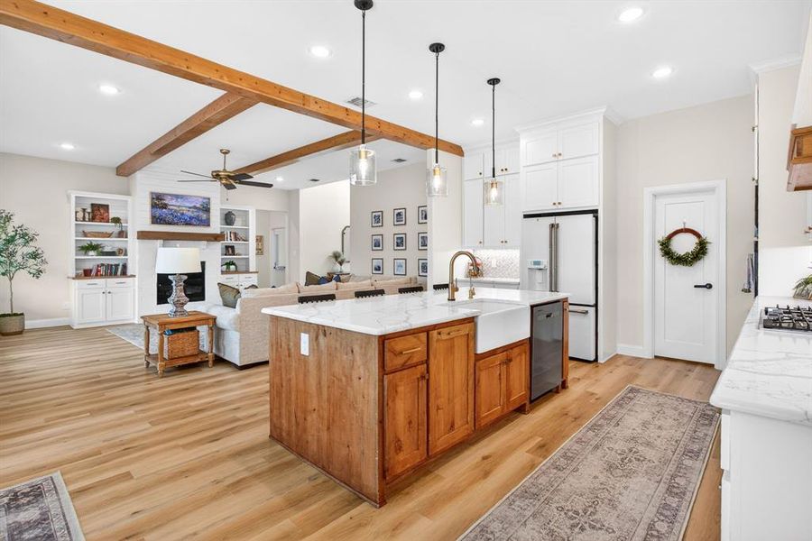 Dual tone kitchen with open floor plan, an island with sink, light stone counters, light wood-style flooring, and beam ceiling Dual tone kitchen with open floor plan, an island with sink, light stone counters, light wood-style flooring, and beam ceiling