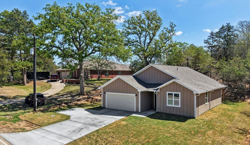 View of front facade featuring a shingled roof, driveway, an attached garage, a front yard, and board and batten siding
