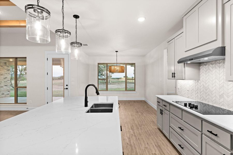 Kitchen with hanging light fixtures, decorative backsplash, light wood finished floors, recessed lighting, and black electric stovetop Kitchen with hanging light fixtures, decorative backsplash, light wood finished floors, recessed lighting, and black electric stovetop