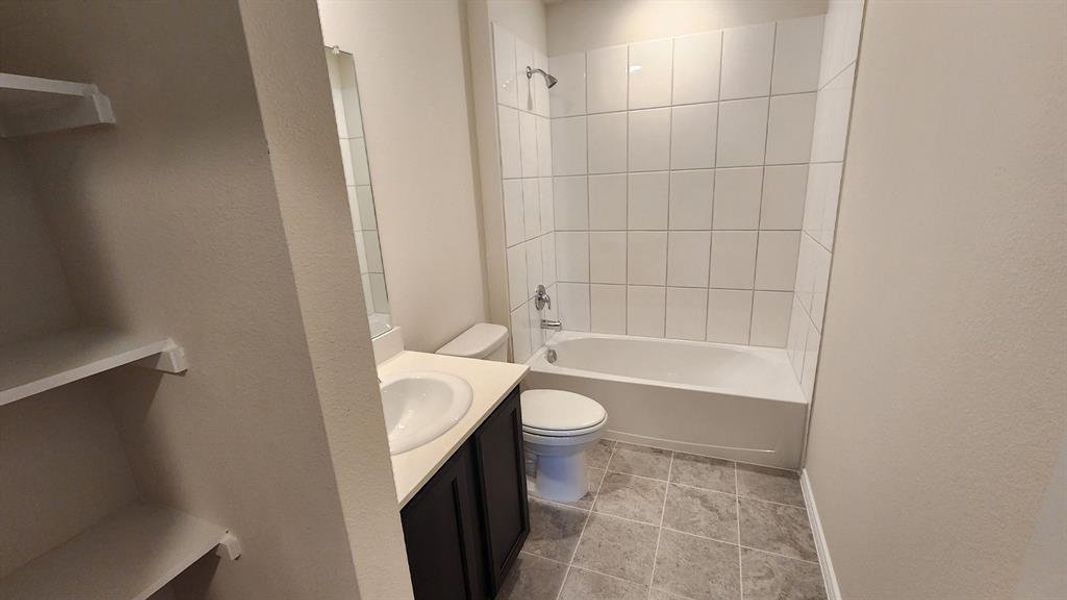 Full bathroom featuring a white porcelain tub and shower combination with white subway tile surround, a dark wood-finish vanity with an integrated sink, and gray tile flooring Full bathroom featuring a white porcelain tub and shower combination with white subway tile surround, a dark wood-finish vanity with an integrated sink, and gray tile flooring
