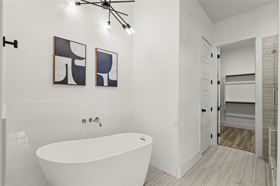 Full bathroom with tile walls, a wainscoted wall, a freestanding tub, a walk in closet, and a shower stall