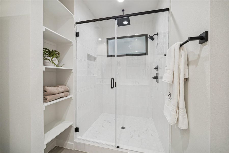 Spacious walk-in shower featuring marble hex tile flooring, dual shower heads, and built-in shelving. Matte black accents and a frameless glass door complete the modern, polished look.