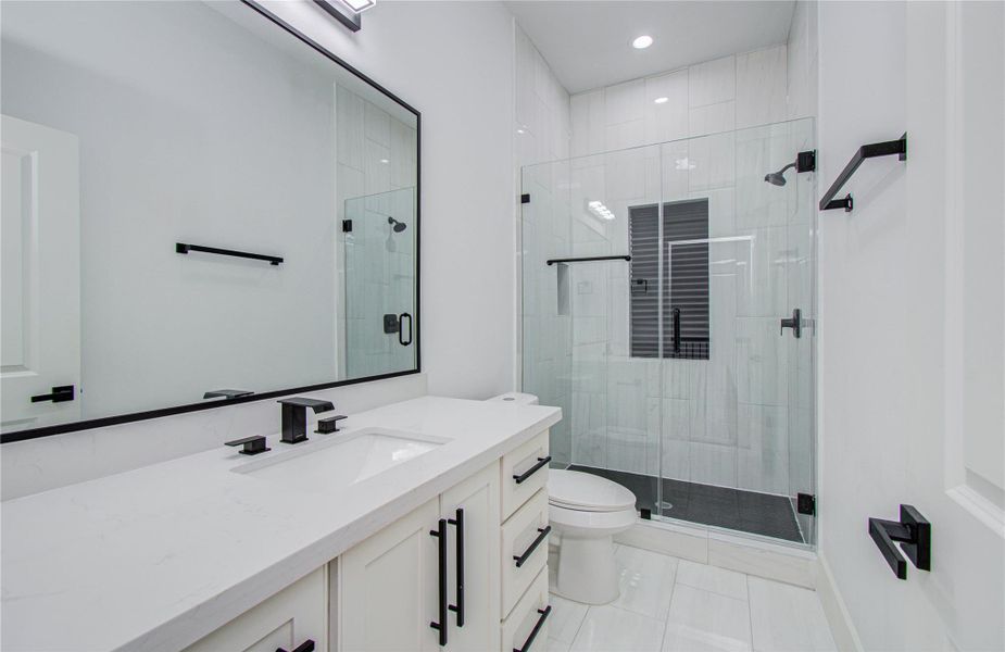 This modern secondary bathroom features a sleek design with a spacious glass-enclosed shower, a large mirror above a white vanity with black fixtures, and bright lighting for a fresh, clean look.