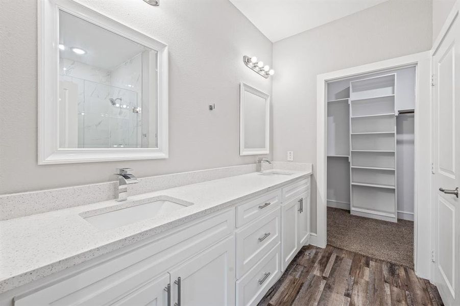 Bathroom featuring a marble finish shower, double vanity, a walk in closet, and dark wood-type flooring Bathroom featuring a marble finish shower, double vanity, a walk in closet, and dark wood-type flooring