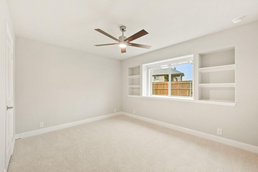 Empty bedroom with carpet, ceiling fan, built-in shelves, and a window overlooking a fenced yard Empty bedroom with carpet, ceiling fan, built-in shelves, and a window overlooking a fenced yard