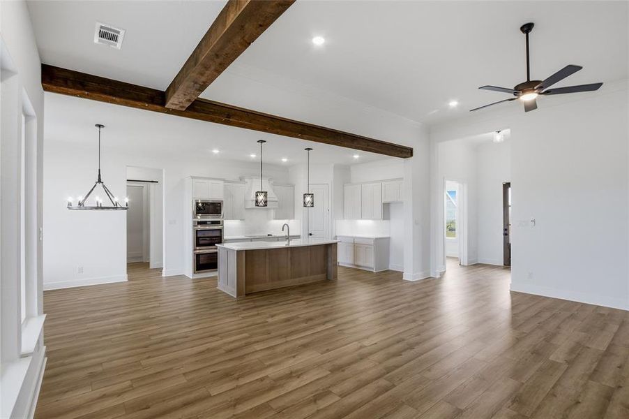 Kitchen featuring open floor plan, a kitchen island with sink, beam ceiling, a ceiling fan, and light wood-type flooring