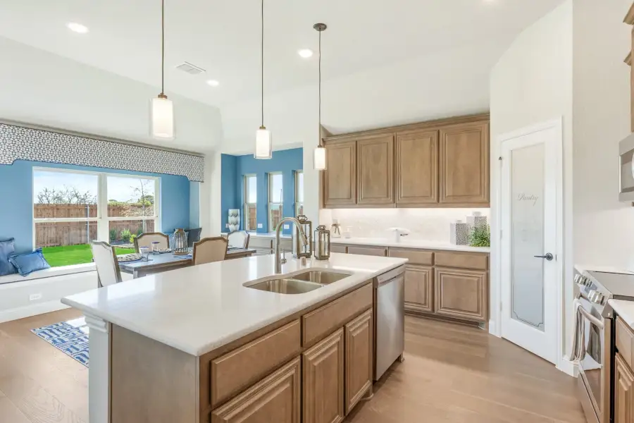 Kitchen with large center island, double sink, brown wood cabinets, and pendant lights open to dining area