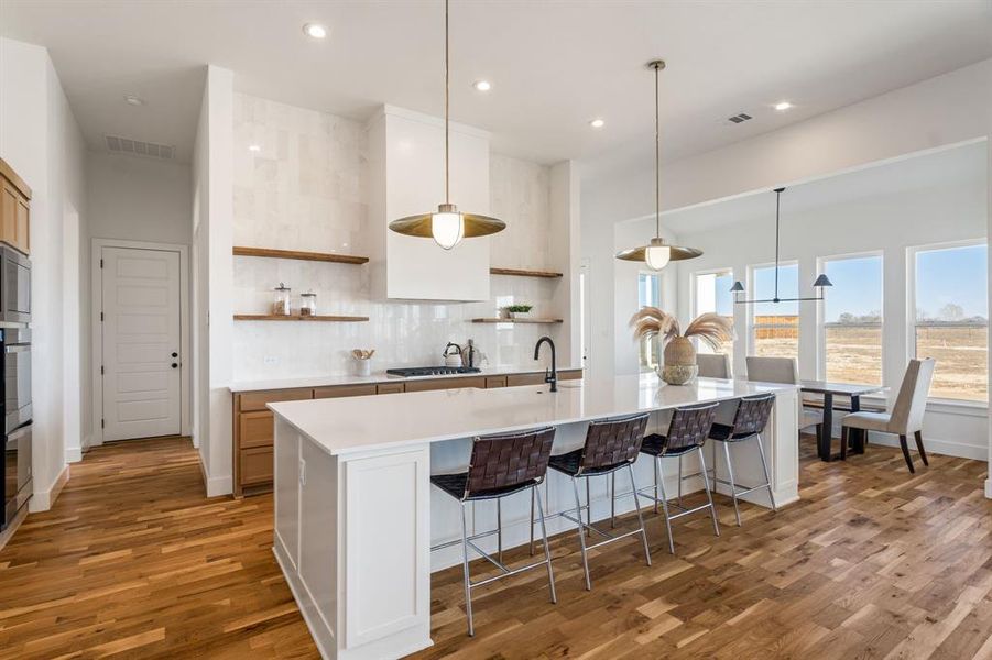 Kitchen with pendant lighting, a breakfast bar area, tasteful backsplash, an island with sink, and dark hardwood / wood-style flooring