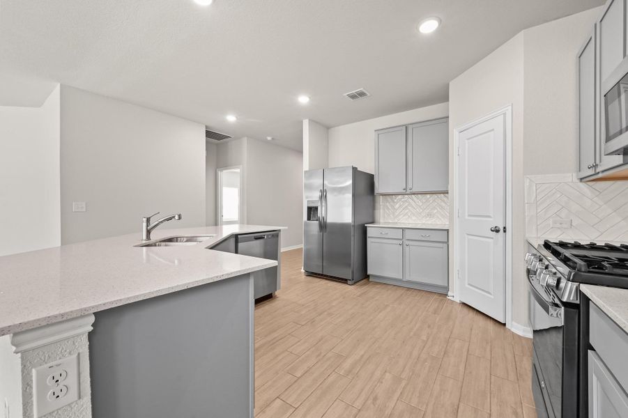 Kitchen with gray cabinets, appliances with stainless steel finishes, light stone countertops, recessed lighting, and backsplash