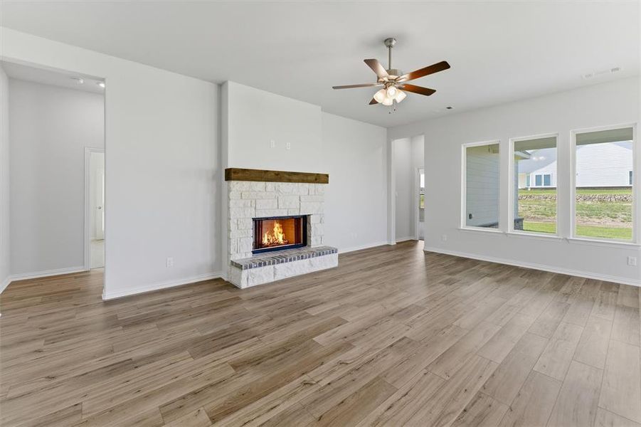 Spacious living area featuring light wood-finish flooring and a stone fireplace with a substantial wood mantel