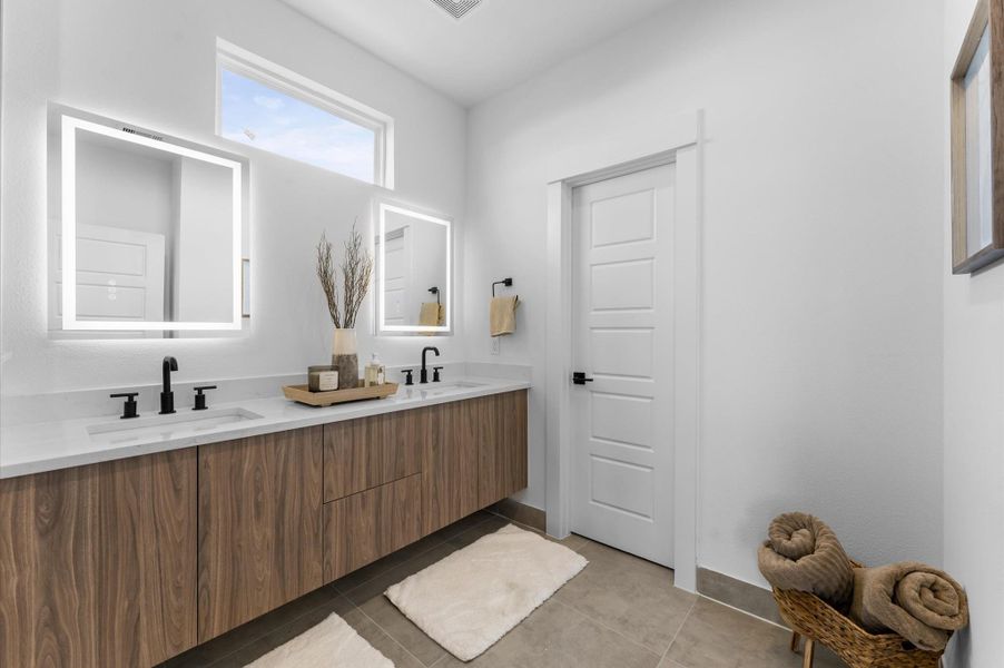 The luxurious primary ensuite features sleek modern finishes, a glass-enclosed shower with stylish tile, and a double-sink vanity topped with quartz countertops, complemented by two contemporary mirrors and lighting fixtures, creating a bright, elegant, and functional retreat.