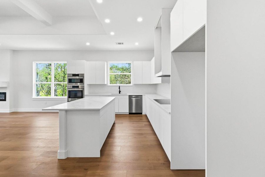 A streamlined culinary space features hardwood floors, recessed lighting, and a substantial island with seating. A streamlined culinary space features hardwood floors, recessed lighting, and a substantial island with seating.