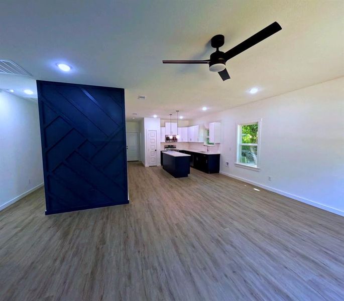 Unfurnished living room with dark wood finished floors, a barn door, ceiling fan, and recessed lighting Unfurnished living room with dark wood finished floors, a barn door, ceiling fan, and recessed lighting