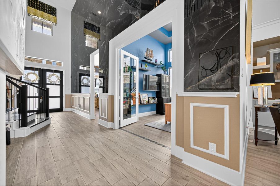This home features a modern, open entryway with high ceilings, elegant tile flooring, and stylish black accents. The space is bright and inviting, with large windows and a unique blue room visible through French doors, adding character and charm. This home features a modern, open entryway with high ceilings, elegant tile flooring, and stylish black accents. The space is bright and inviting, with large windows and a unique blue room visible through French doors, adding character and charm.
