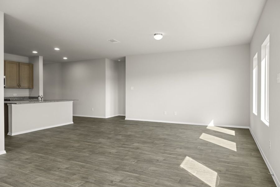 Image of home living area with wood-look floors, white walls, windows on one side and kitchen on the other