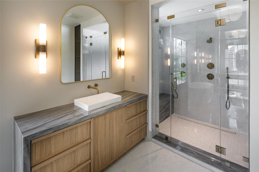 The shower deserves its own moment. Oversized glass, full-height stone, multiple shower heads and hand sprays, brass hardware, and a built-in bench turn an everyday necessity into something considerably better.