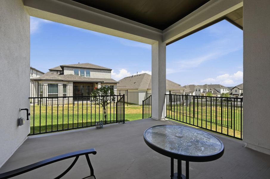 Concrete flooring and structural columns frame a covered back porch overlooking a fenced lawn.