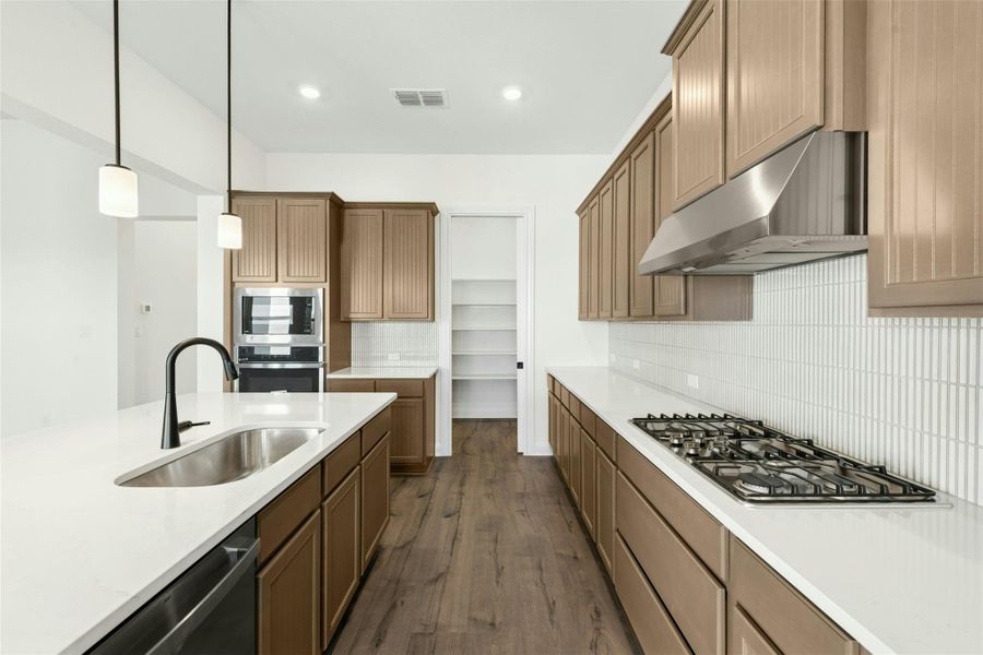 Kitchen with wood finish cabinetry, dark wood-style flooring, pendant lighting, backsplash, and stainless steel appliances