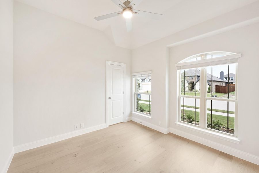 Empty bedroom with hardwood floors, ceiling fan, and large arched windows overlooking a neighborhood
