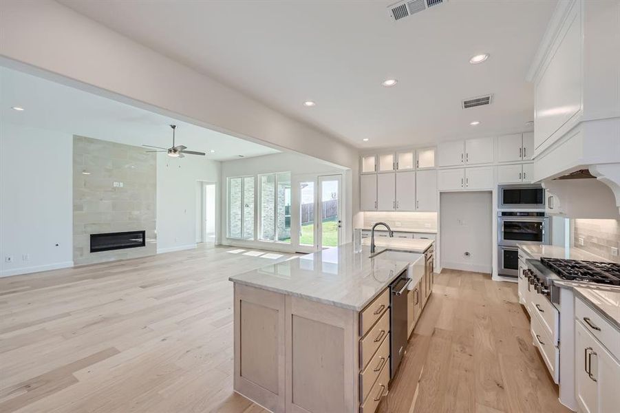 Kitchen with an island with sink, backsplash, white cabinets, appliances with stainless steel finishes, and light hardwood / wood-style floors