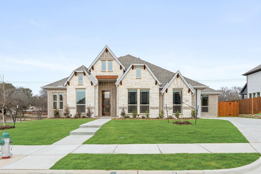 Single-story home with stone and brick exterior, pitched roof, large windows, and green front lawn Single-story home with stone and brick exterior, pitched roof, large windows, and green front lawn