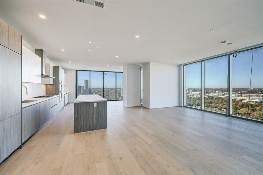 This is a modern, open-concept living space featuring a spacious kitchen with sleek  Pedini cabinetry and a central island, porcelain counter tops and back splash complemented by light hardwood flooring throughout and ample natural light from large windows.