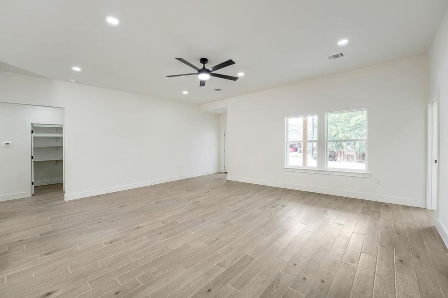 A spacious, naturally illuminated room features light wood flooring and contemporary recessed lighting.