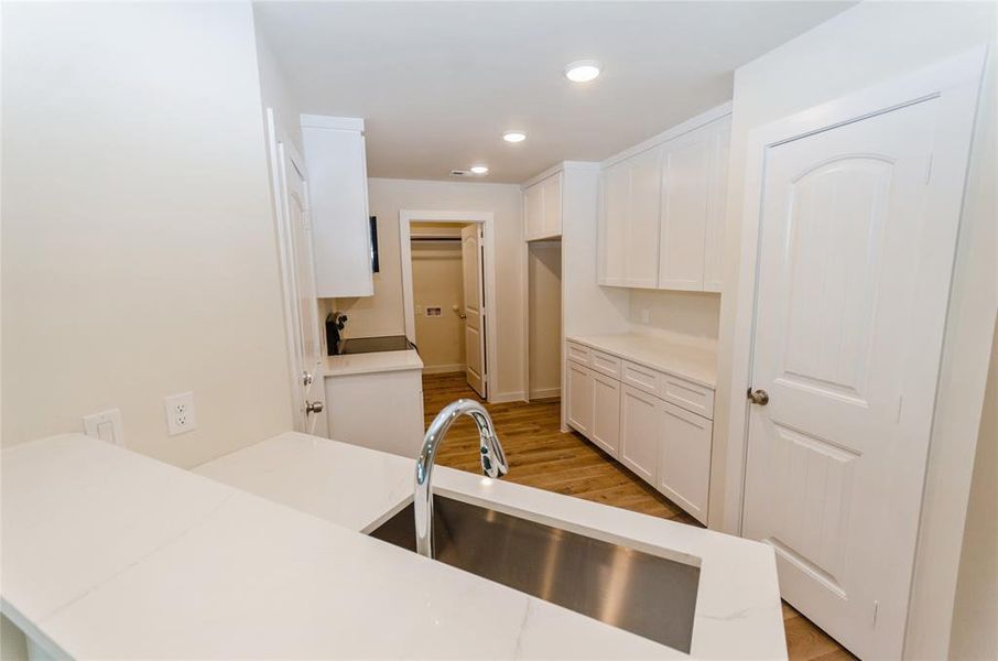 Kitchen with white cabinets, kitchen peninsula, light wood-type flooring, and sink