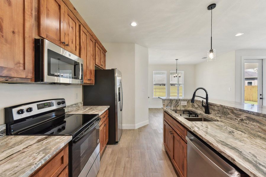 Kitchen with brown cabinets, light stone countertops, stainless steel appliances, and a sink