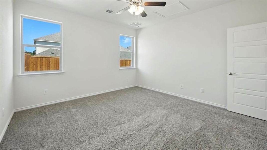 Empty room featuring carpet flooring, attic access, and a ceiling fan