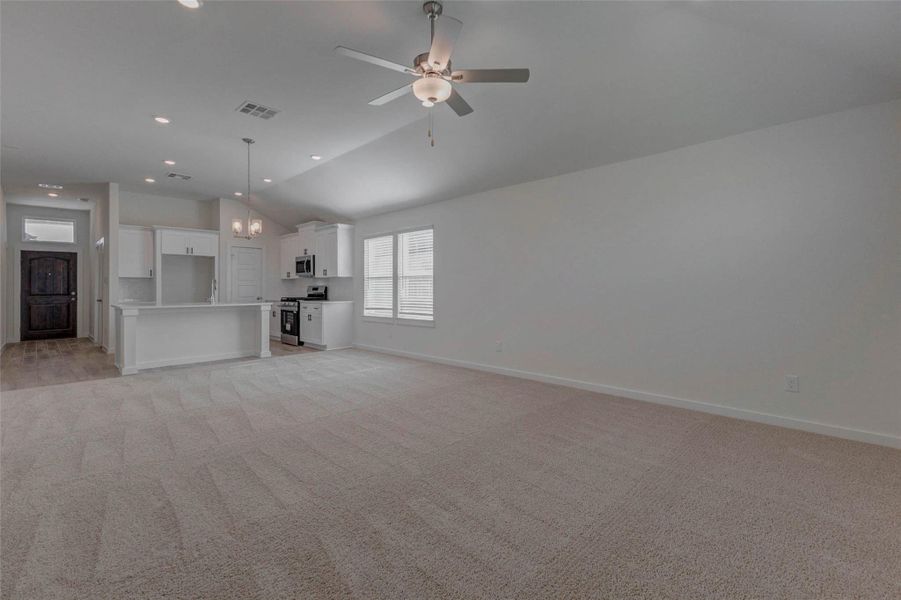 From this wide-angle view, the heart of the home comes alive highlighting the bright and airy layout, central island with pendant lighting, and an expansive family room ideal for entertaining. A ceiling fan and large windows ensure airflow and sunlight, while the open floorplan supports flexibility for living, dining, and gathering.