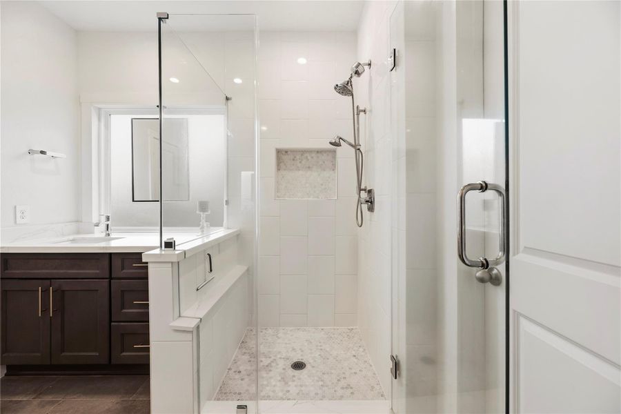 Enlarged primary walk-in shower with thick frameless glass, tile surround and a built-in niche and shelf.