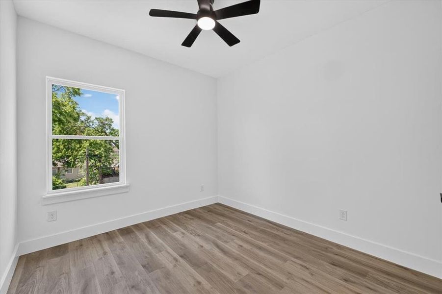 Room featuring wood-finish flooring, a double-hung window, a ceiling fan with integrated lighting, white walls, and white baseboards Room featuring wood-finish flooring, a double-hung window, a ceiling fan with integrated lighting, white walls, and white baseboards