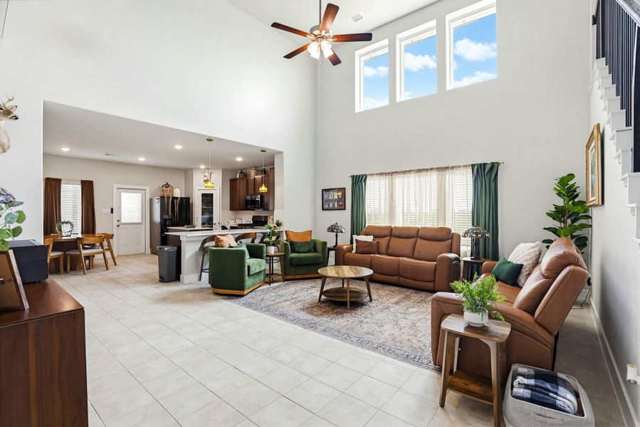 Two-story living area featuring a vaulted ceiling with a ceiling fan, three transom windows, and an open-concept design to the kitchen and dining areas
