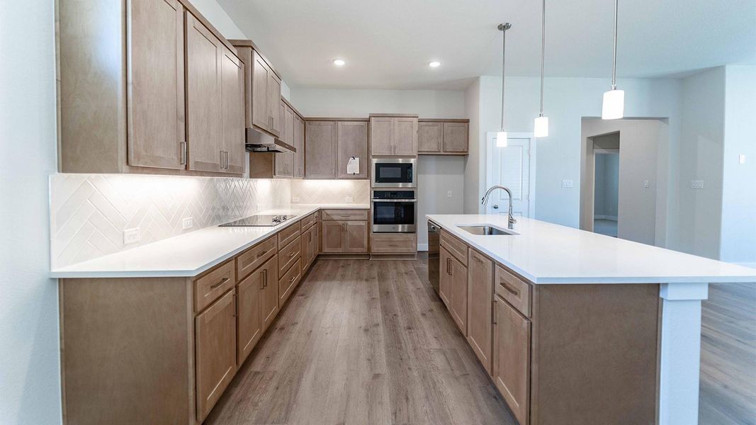 Kitchen featuring decorative backsplash, light wood-style flooring, oven, decorative light fixtures, and a center island with sink Kitchen featuring decorative backsplash, light wood-style flooring, oven, decorative light fixtures, and a center island with sink
