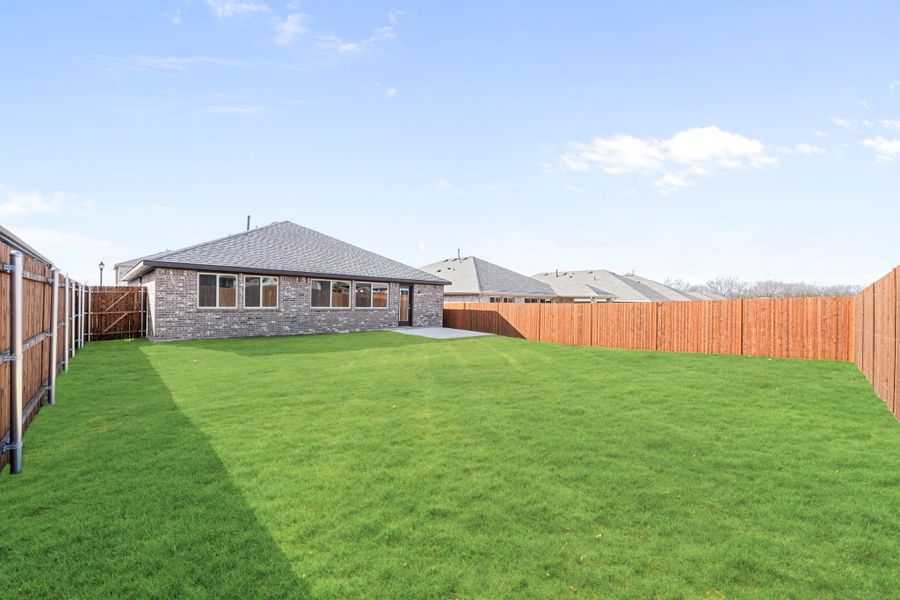 Backyard with large green lawn, brick home, and wood privacy fence on three sides Backyard with large green lawn, brick home, and wood privacy fence on three sides
