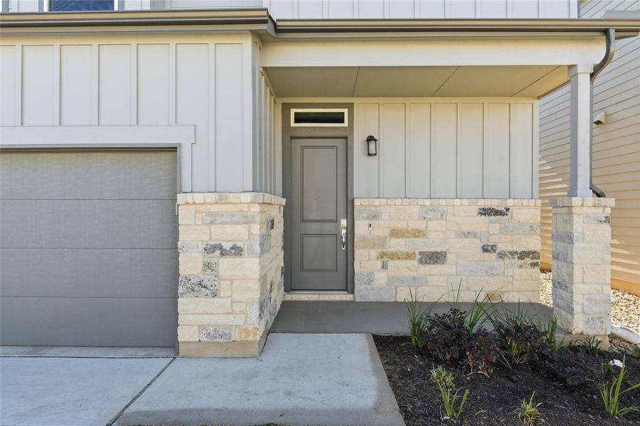 View of exterior entry with board and batten siding, stone siding, covered porch, and a garage View of exterior entry with board and batten siding, stone siding, covered porch, and a garage