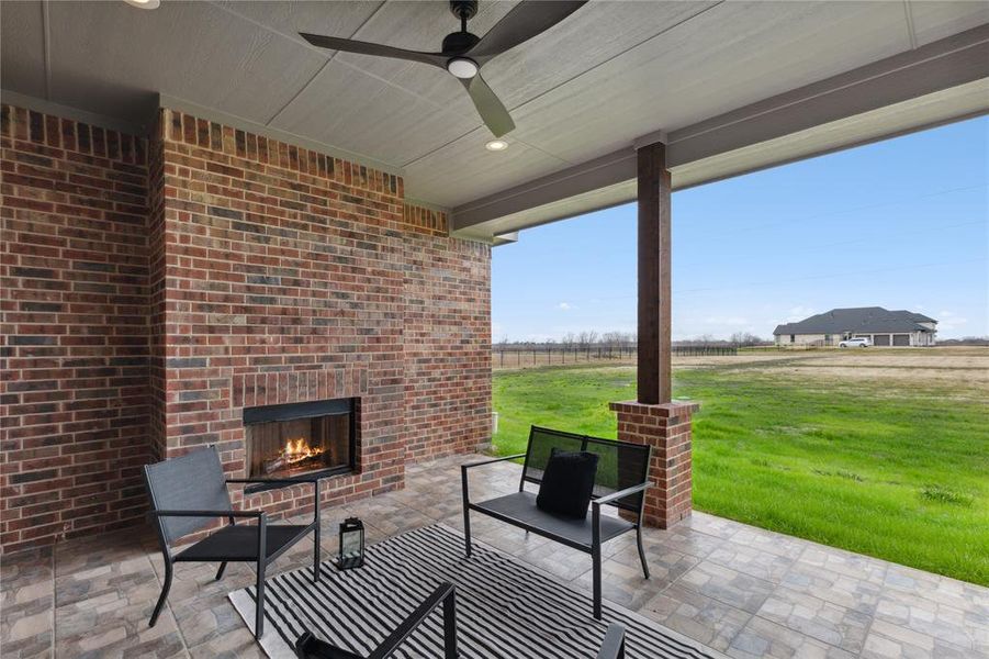 View of patio with an outdoor brick fireplace, ceiling fan, and a rural view