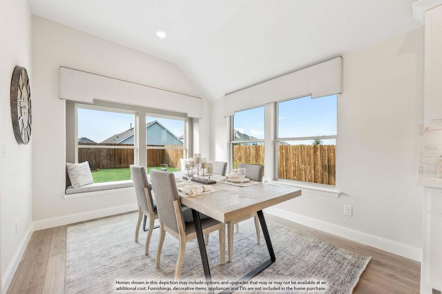 Bright dining room with wood table, gray chairs, vaulted ceiling, window seat, and large windows overlooking backyard