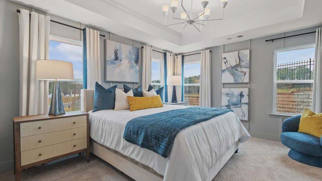 Stylish primary suite in new construction townhome featuring tray ceiling and bright modern palette in Riverdale, GA.