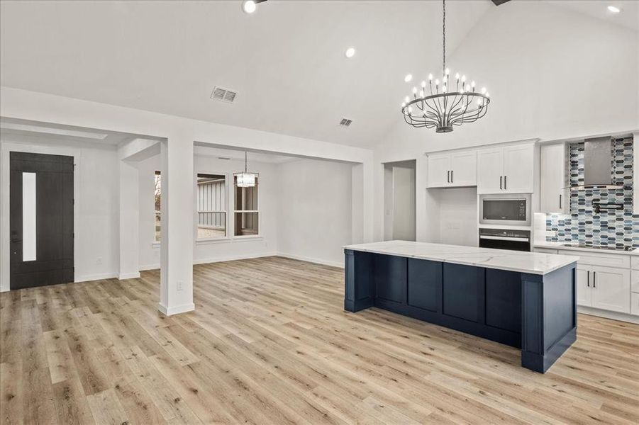 Kitchen with tasteful backsplash, hanging light fixtures, stainless steel microwave, wall oven, and white cabinets