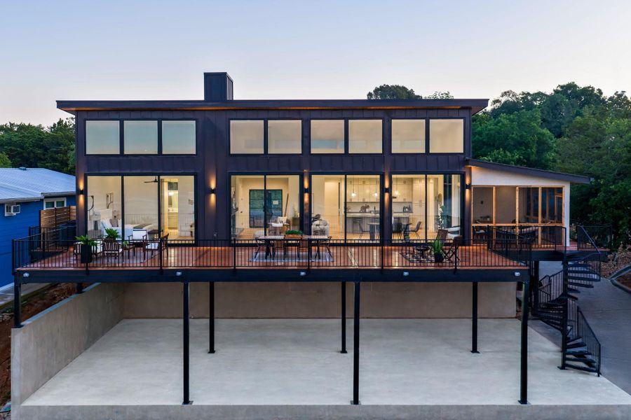 Multi-level modern residence featuring an expansive rear deck with dark metal railings, a screened-in porch, and a spiral staircase Multi-level modern residence featuring an expansive rear deck with dark metal railings, a screened-in porch, and a spiral staircase