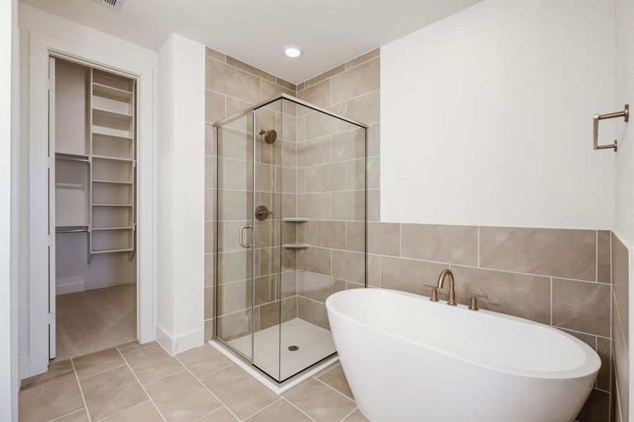 Contemporary bathroom featuring a freestanding soaking tub, glass-enclosed shower, neutral tile surround, recessed lighting, and a walk-in closet with built-in shelving