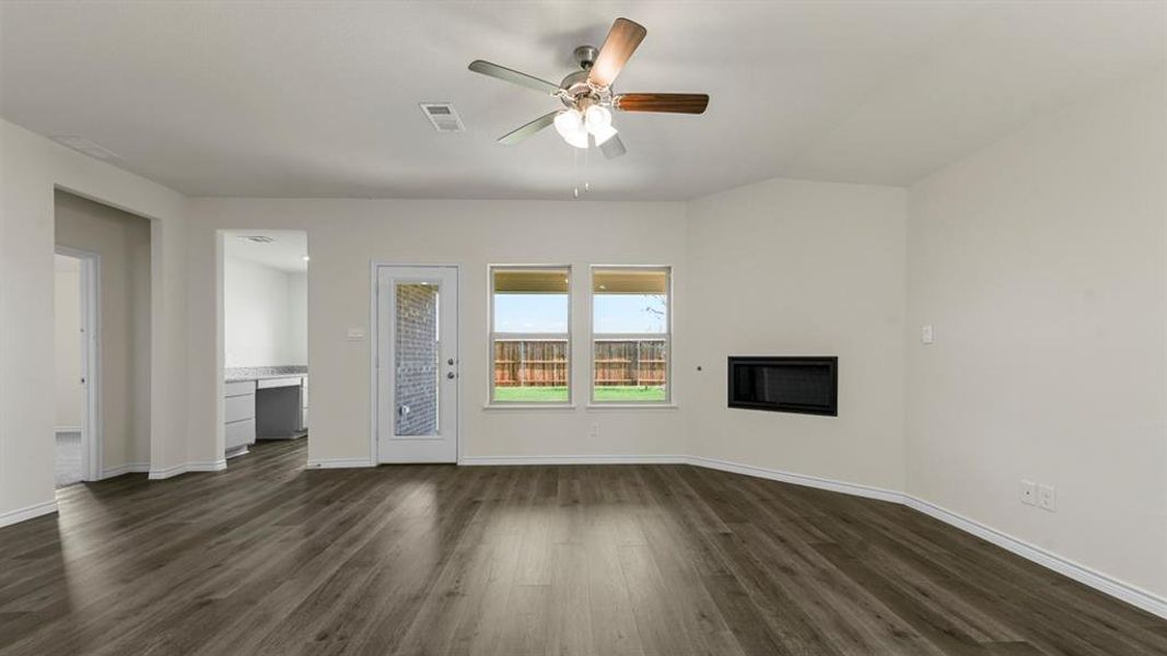 This open living area features wood-look flooring, a ceiling fan, and a wall-mounted fireplace