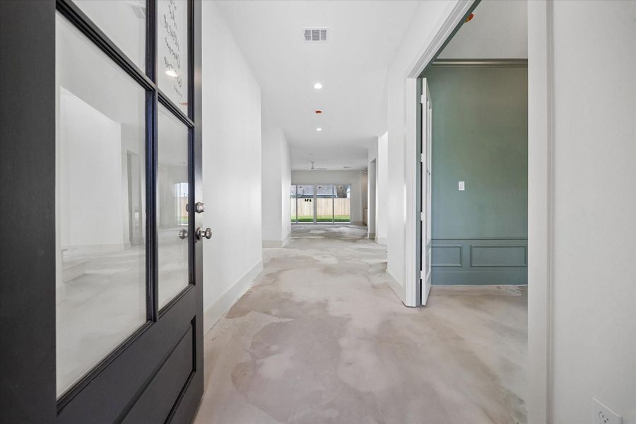 Welcoming entry with modern glass front door opens to a long, light filled hallway that immediately showcases the home’s clean lines and open concept layout. High ceilings, recessed lighting, and wide plank flooring create a bright and airy feel, while the sightline extends straight to the backyard through expansive glass doors.